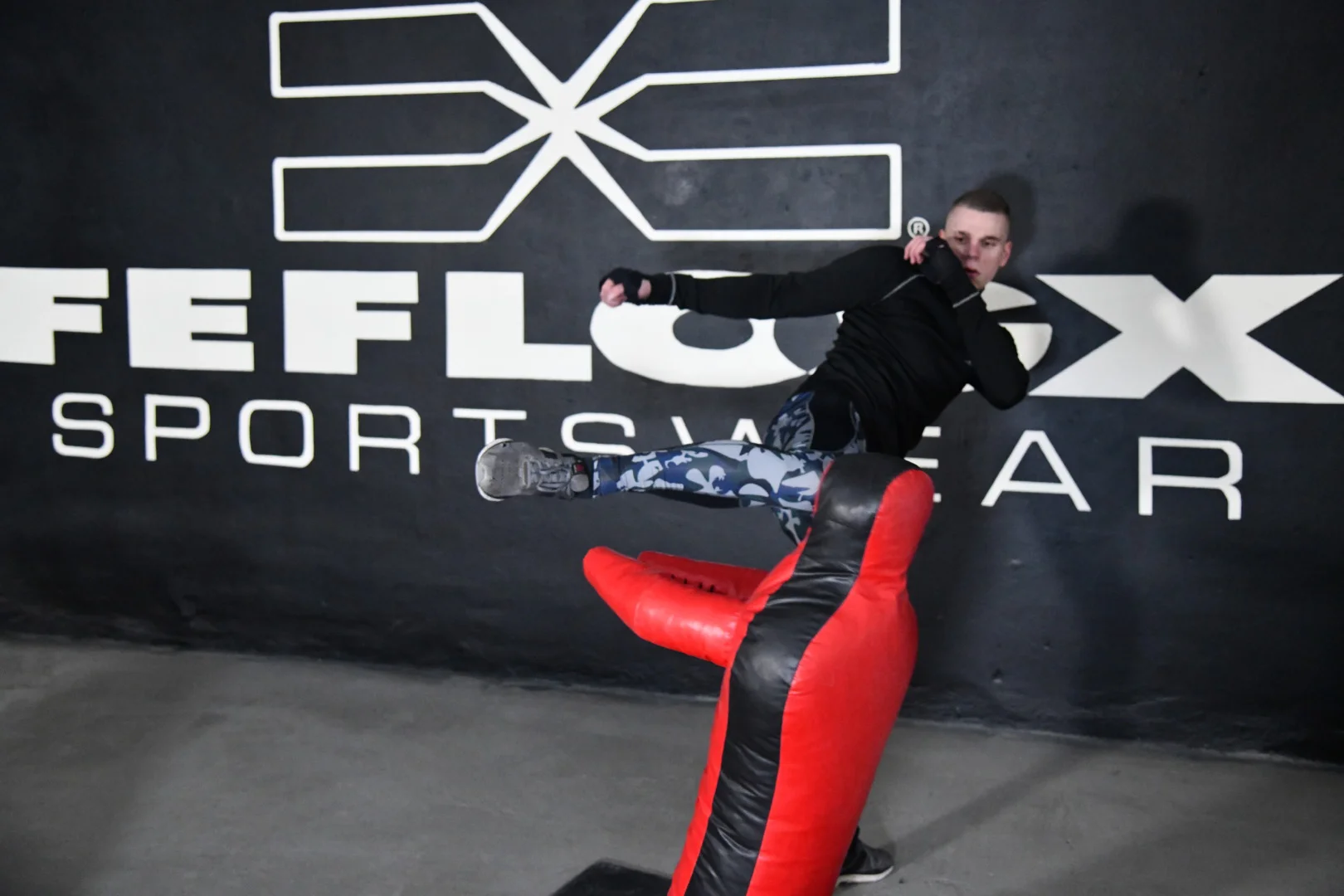 FEFLOGX, MMA-Training & Urban Functional Fitness Shooting in FFX Sport Leggings Camouflage, FFX Sport Shorts, FFX Boxbandagen & Sport Sweater, Fitness Longsleeve mit Kampfsport Dummy & Sport Reifen mit Hammer schlagen, Side-Kick / Round-House-Kick zum Kopf, KO-Tritt Kickboxen in Industrie Ruine in Frankfurt am Main, mit FEFLOGX Logo-Graffiti an der Wand (6).